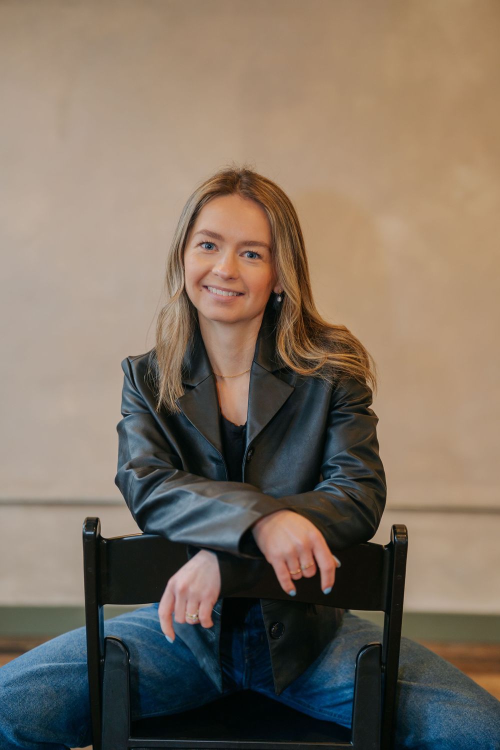 Professional portrait series showing person in black blazer and jeans seated on dark wooden chair against neutral backdrop.