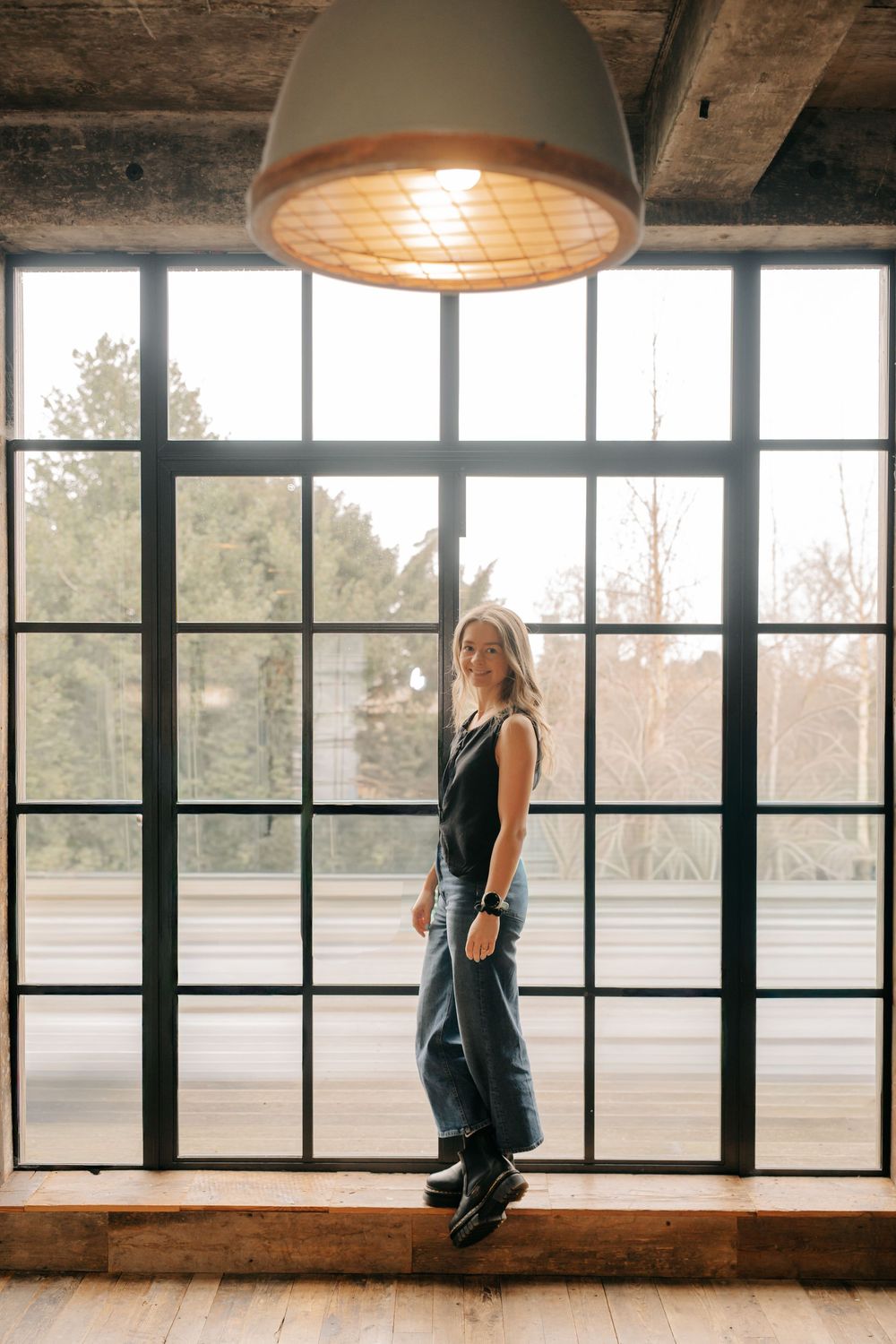 A person sits on a windowsill in a rustic room with large windows overlooking a scenic view, captured in a triptych style.
