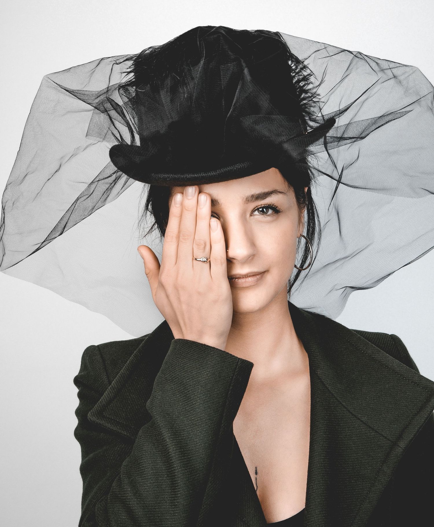 Fine Art Fotografie, dramatic fashion portrait of a woman with a black hat with tulle veil, dark jacket, against a light background.