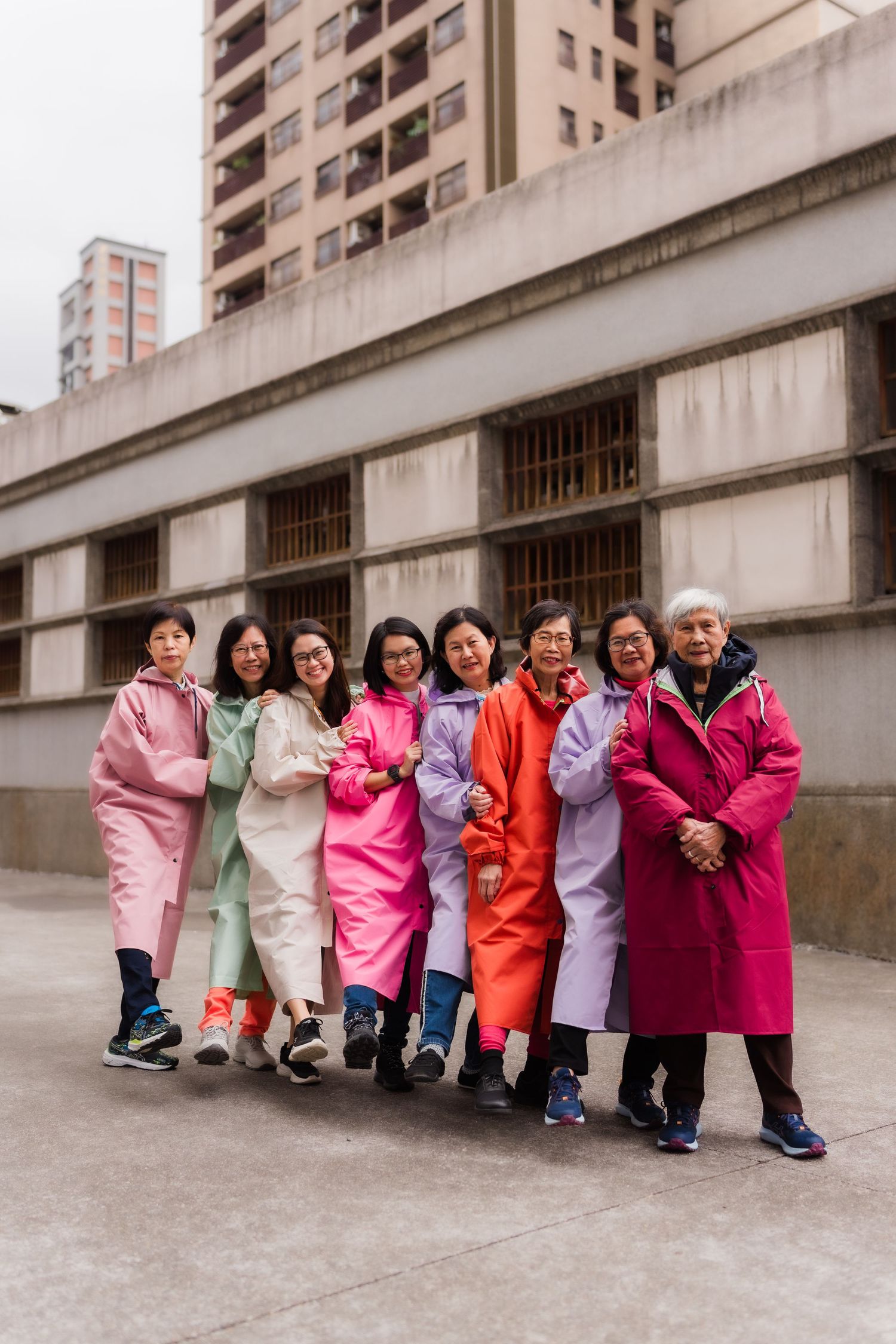 A group poses in colorful winter coats against an urban concrete building backdrop in Taiwan.
