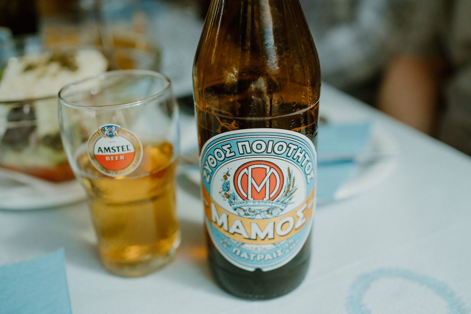 A bottle of Mamos craft beer with an Amstel glass filled with golden lager on a white tablecloth.
