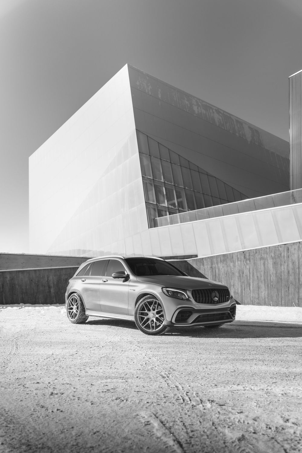 Mercedes-Benz GLC AMG in silver parked in front of modern angular architecture in black and white.