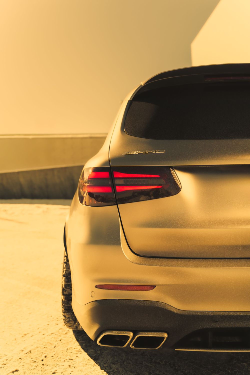 Close-up shot of a luxury car's rear end with LED taillights and dual exhaust tips in warm golden light.