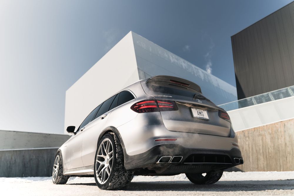 Silver Mercedes GLC SUV with custom black wheels parked in front of modern white building.