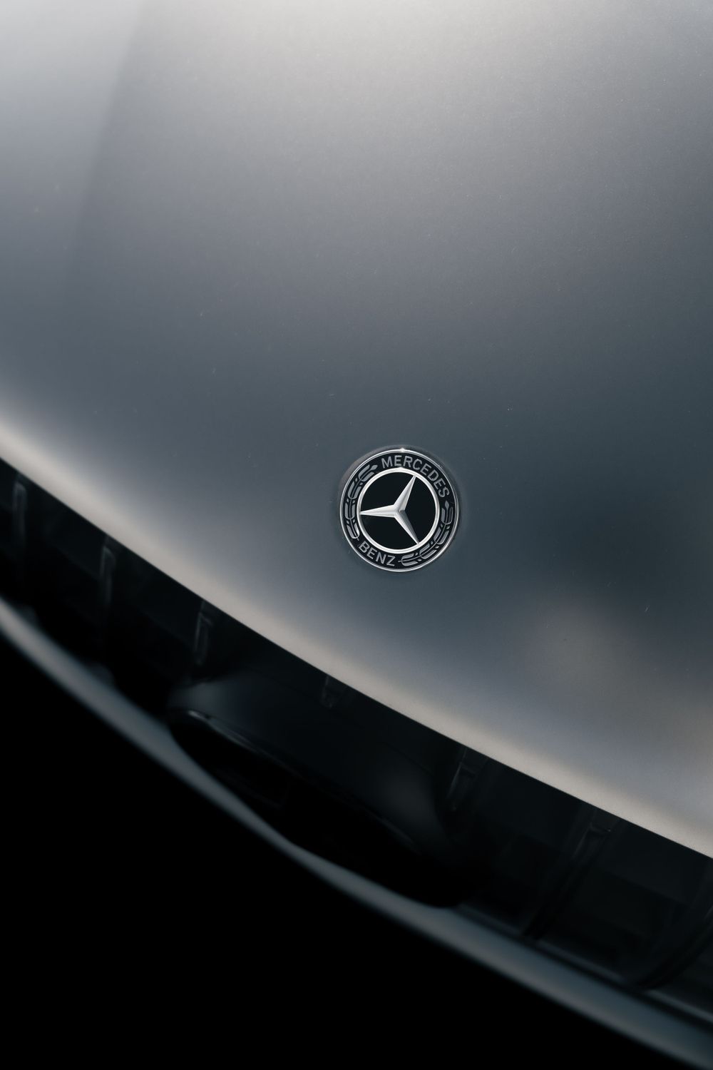 Close-up shot of a Mercedes-Benz emblem on a sleek silver car hood in dramatic lighting.