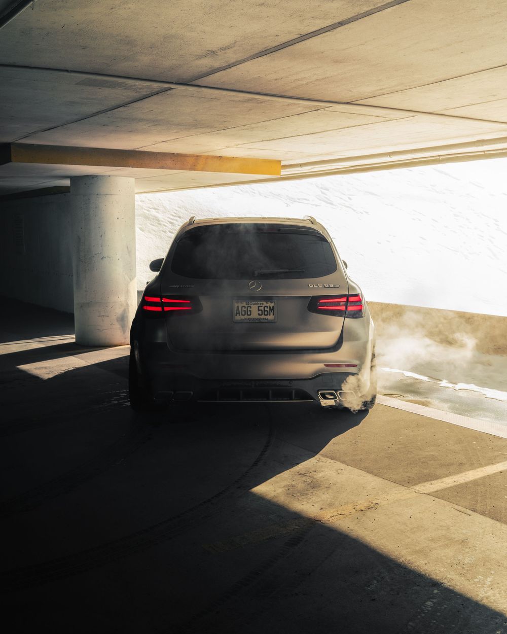 A black Mercedes-Benz wagon parked in a dimly lit concrete parking garage with dramatic sunlight streaming in.