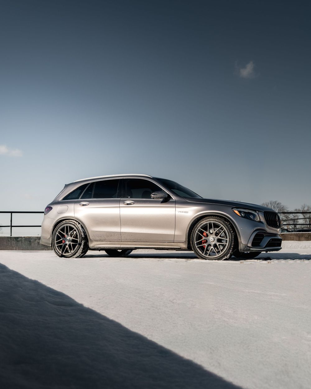 A silver Mercedes-Benz GLC SUV parked on a rooftop against a moody blue sky with custom black alloy wheels.