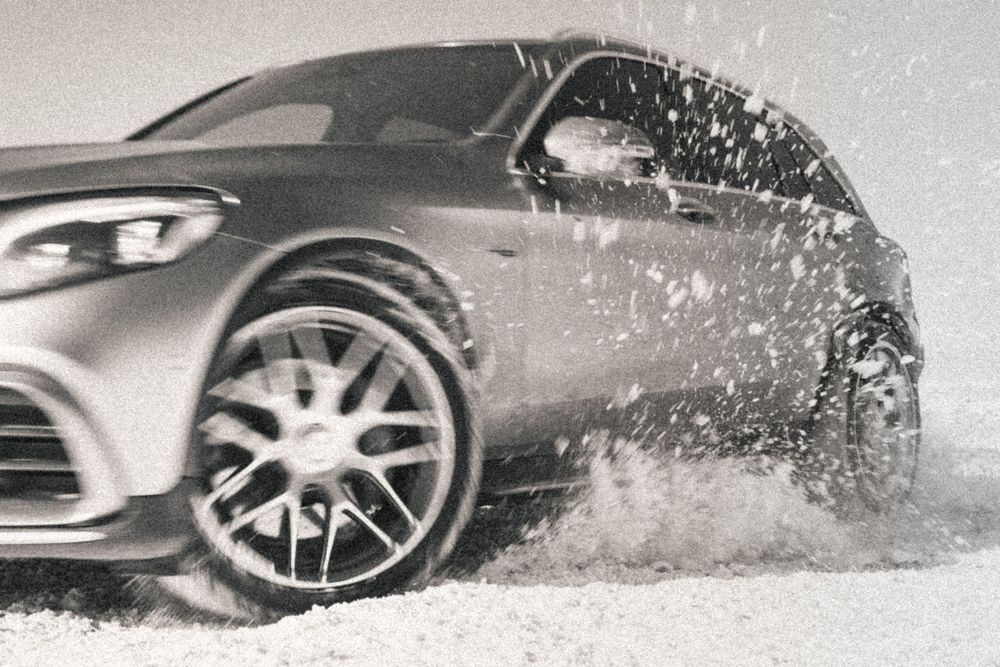 Modern luxury vehicle in metallic gray splashing through water with snow or dirt, emphasizing its sporty alloy wheels.