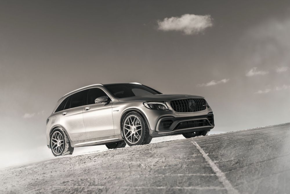 Mercedes-AMG GLC SUV in silver stands on hill against dramatic monochrome sky.