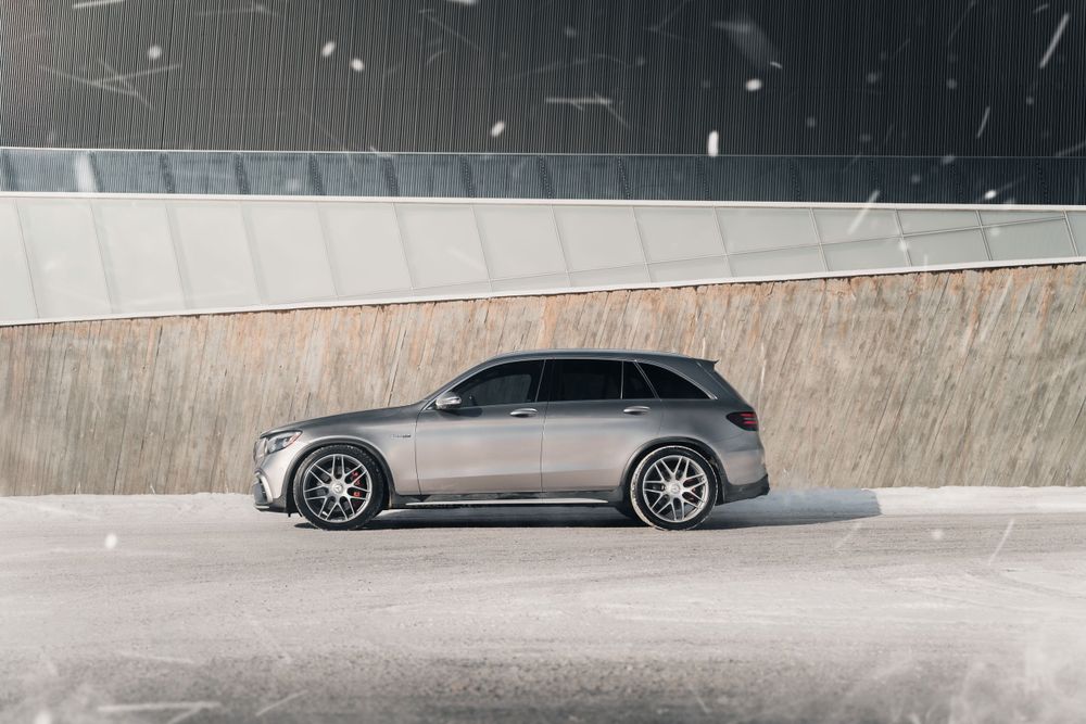 A sleek gray Mercedes-Benz GLC SUV parked next to a concrete wall in snowy conditions.