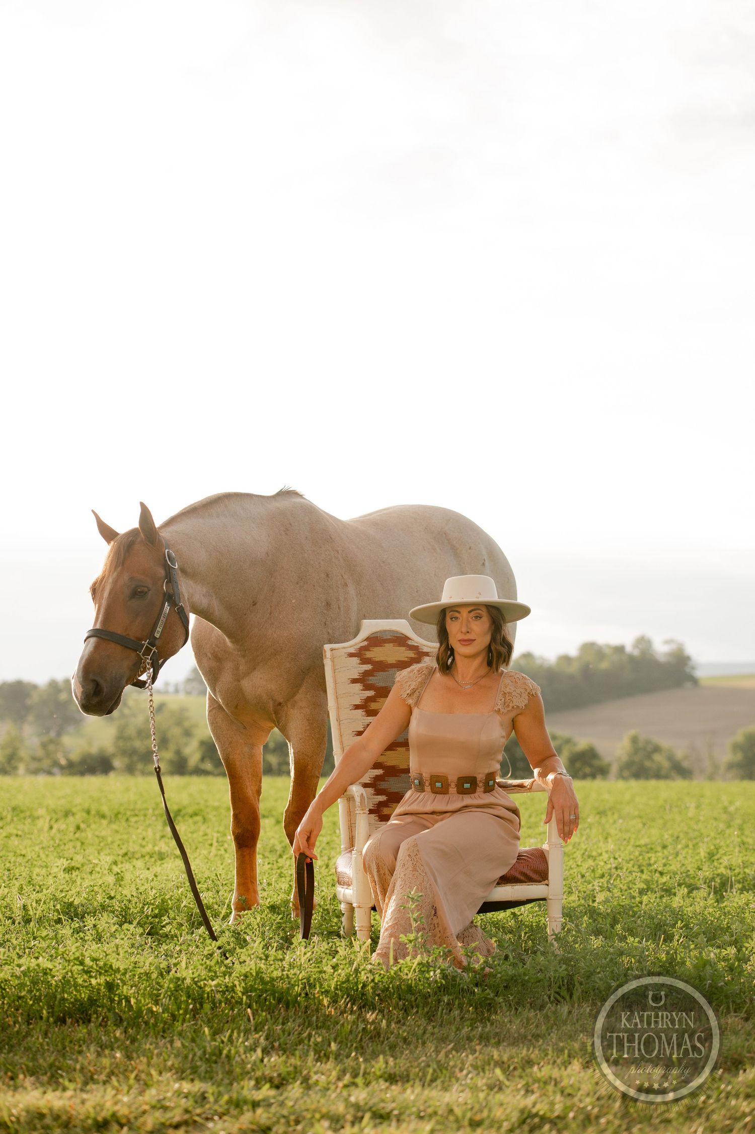 A peaceful scene with a brown horse and person in western wear in a sunny meadow.