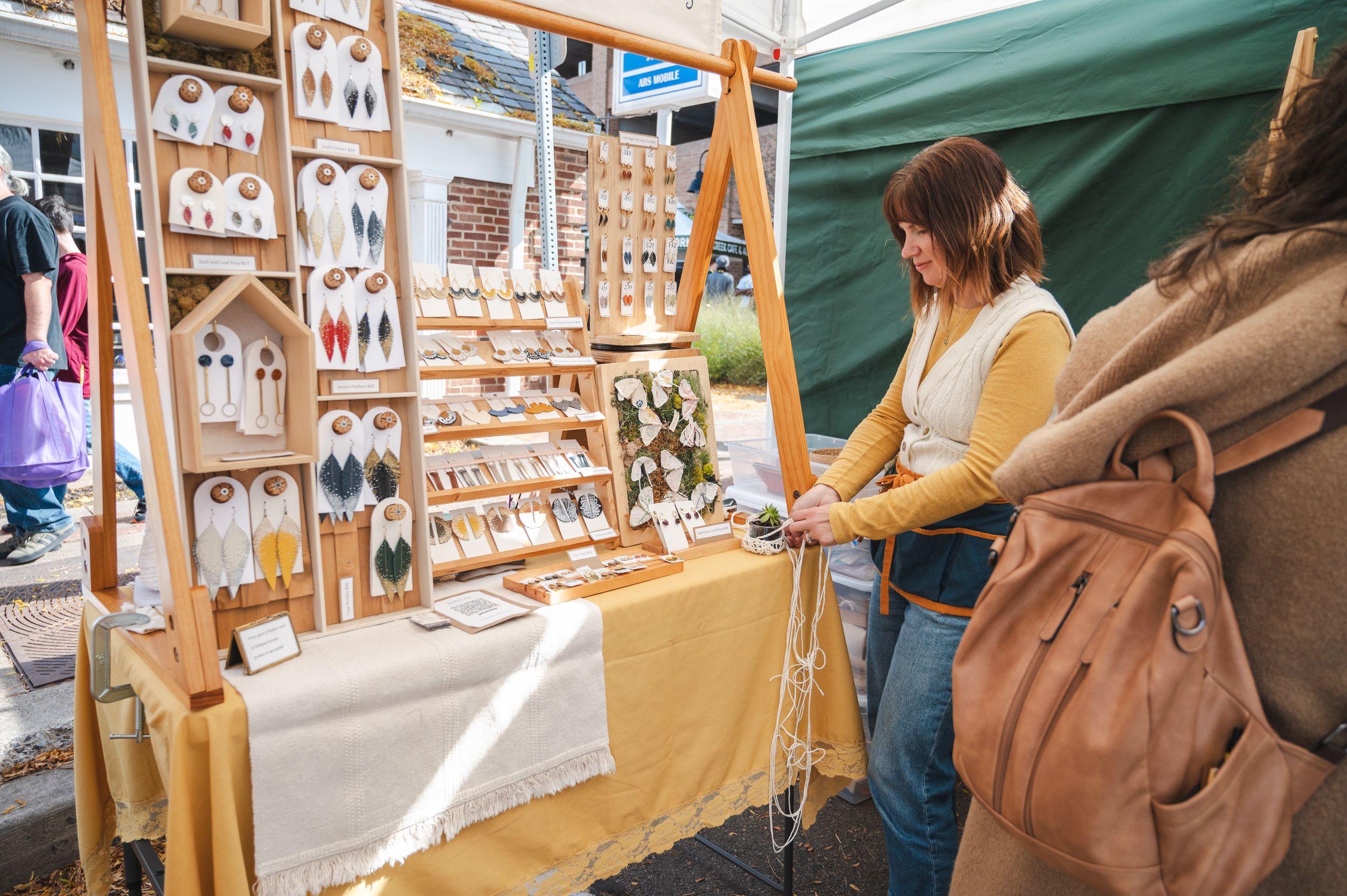 Vendor displays handmade jewelry and accessories at an outdoor craft market booth.