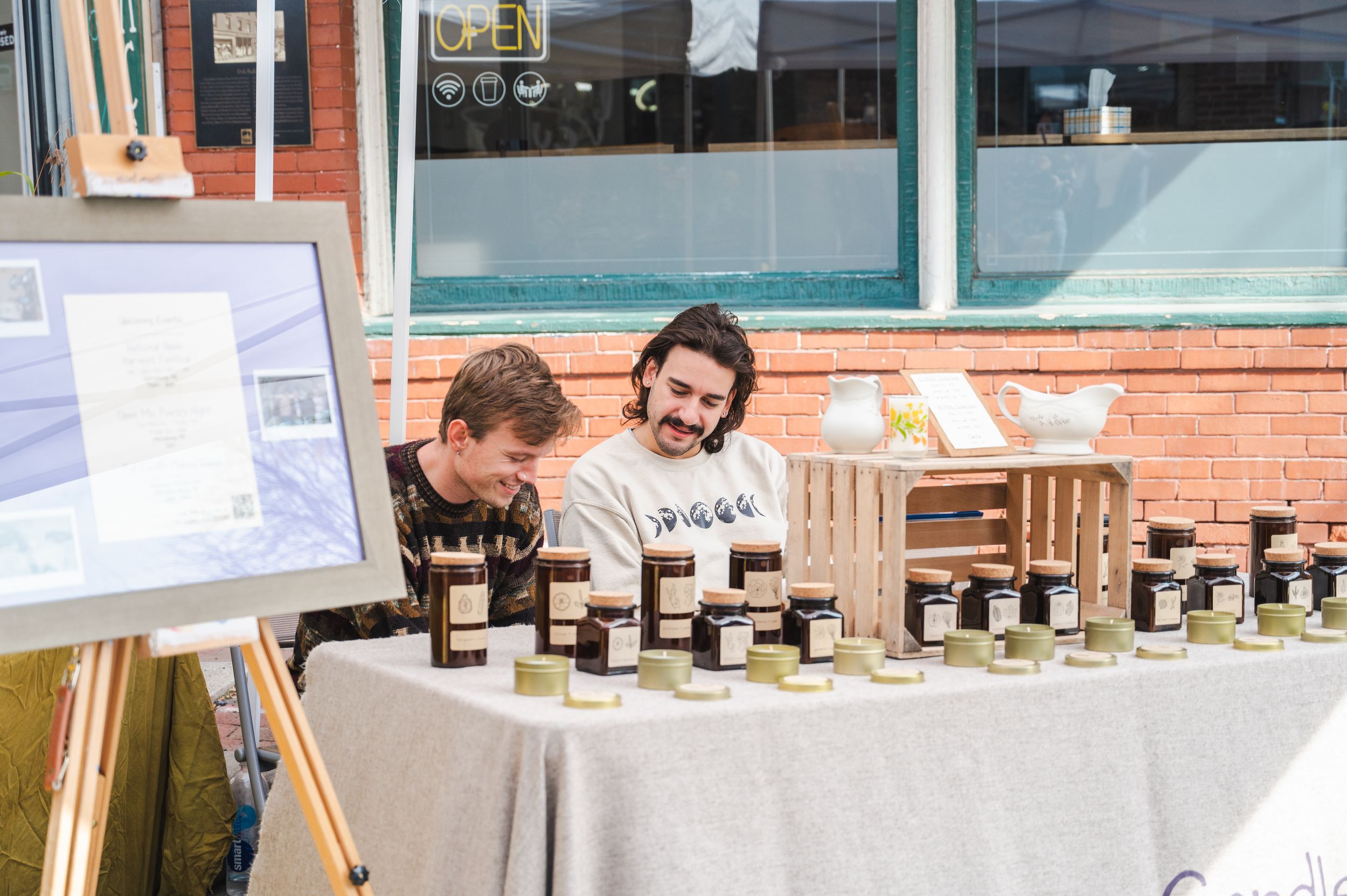 Vendors selling local honey products at outdoor market table display.
