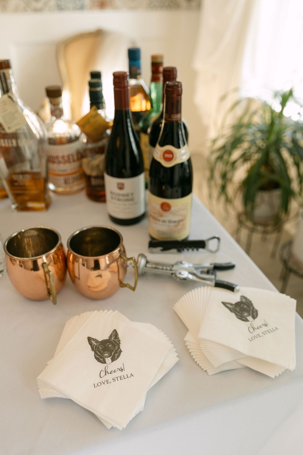 Wedding bar setup with copper mugs, wine bottles and cocktail napkins featuring a wolf logo on a white surface.