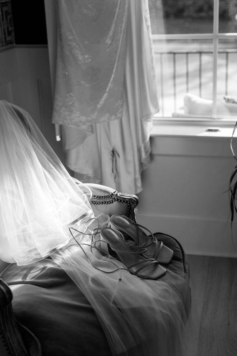 Wedding veil and bridal shoes arranged on a windowsill in black and white.