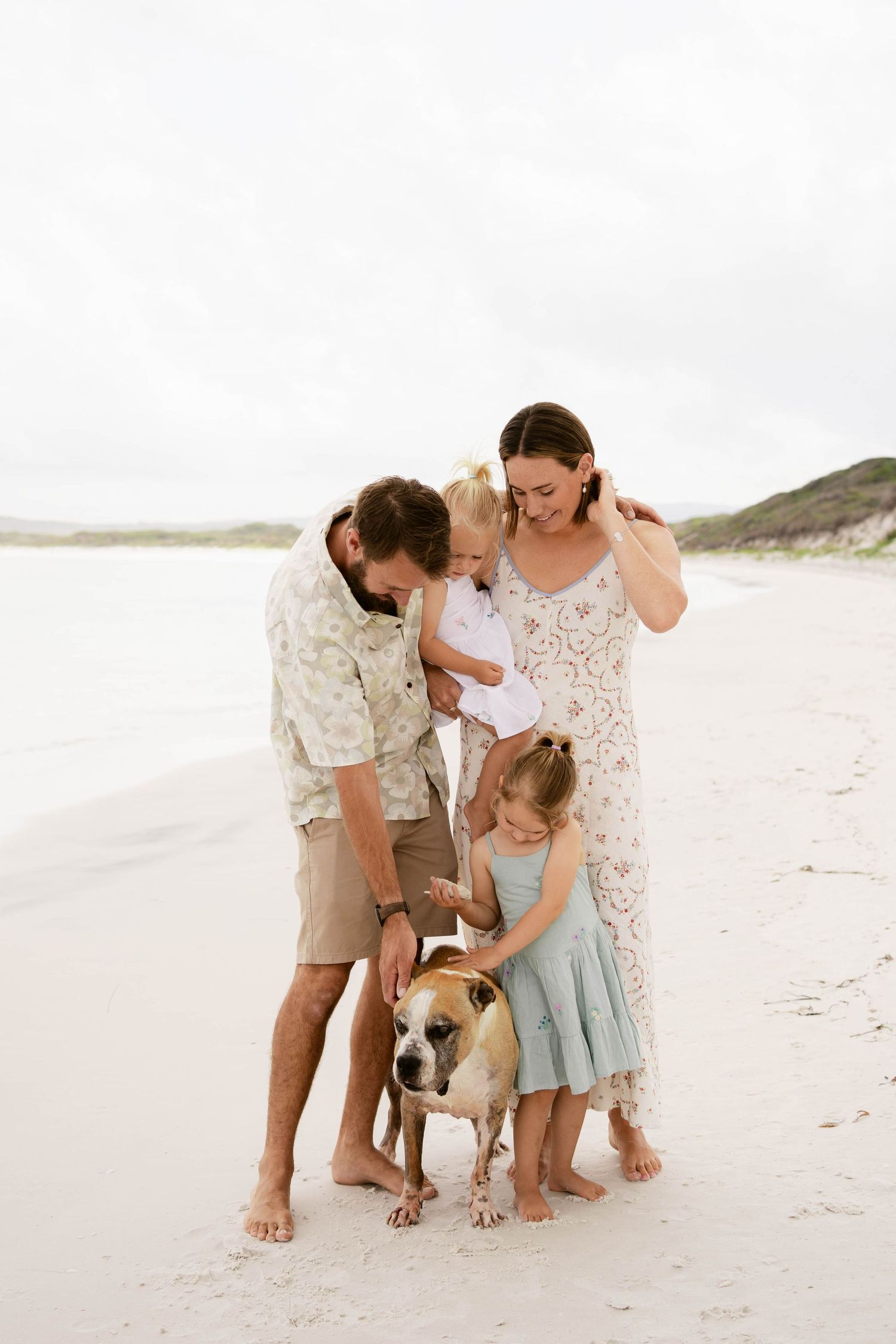 Family and dog share a happy moment together on a white sandy beach.