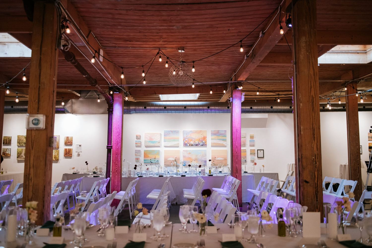 Wedding reception venue with wooden beams, string lights, and purple decor details.