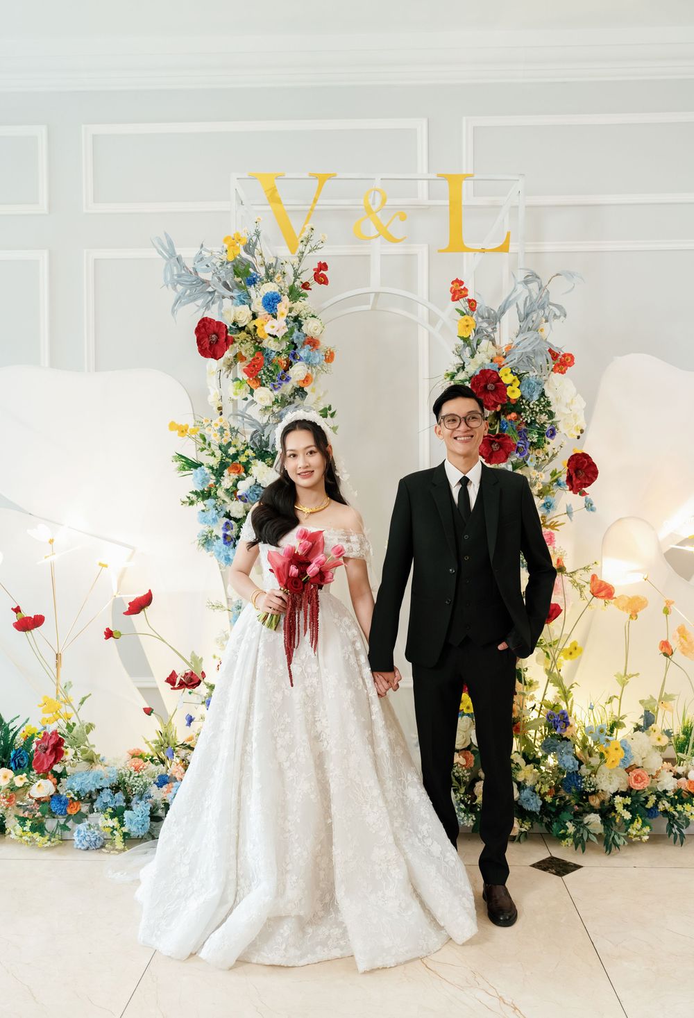 Wedding portrait with floral arch featuring yellow letters and colorful flower arrangements.