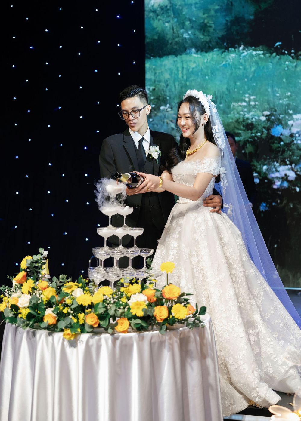 Wedding reception scene with champagne tower and yellow floral decorations against starlit backdrop.