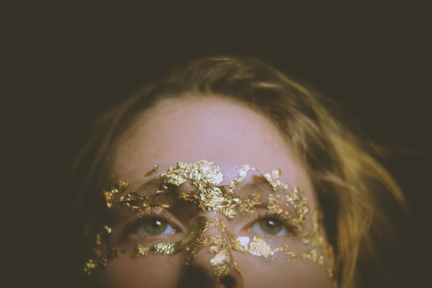 Close up of glittering gold leaf makeup adorning someone's eyebrows and bridge of nose in artistic beauty shot.