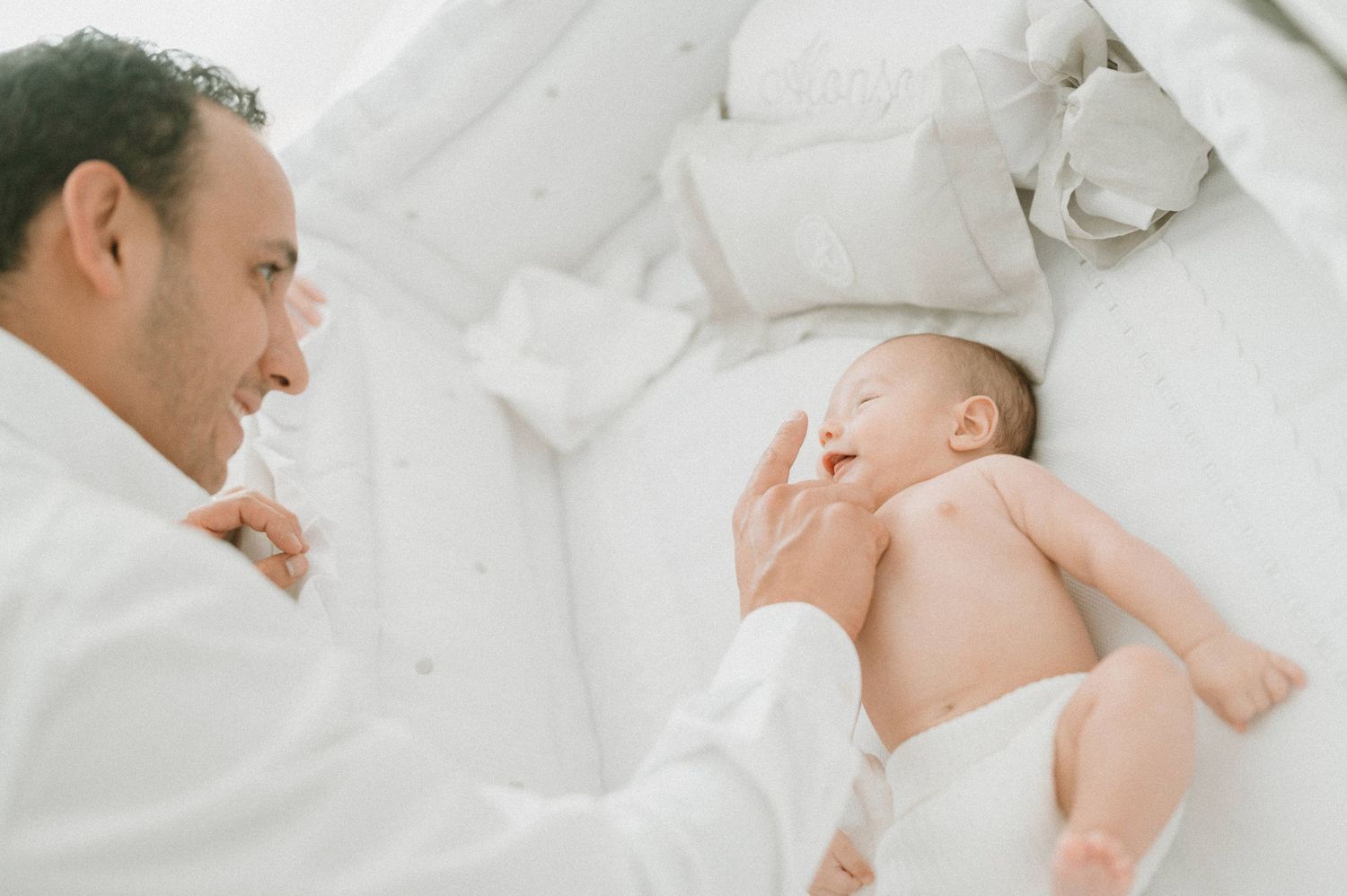 Intimate moment between parent and baby on white bedding.