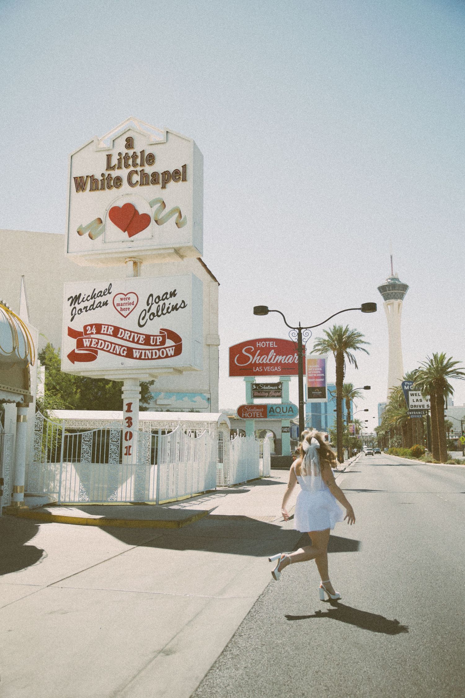 A bride spins in a short white dress outside the Little White Chapel on a sunny Las Vegas day.