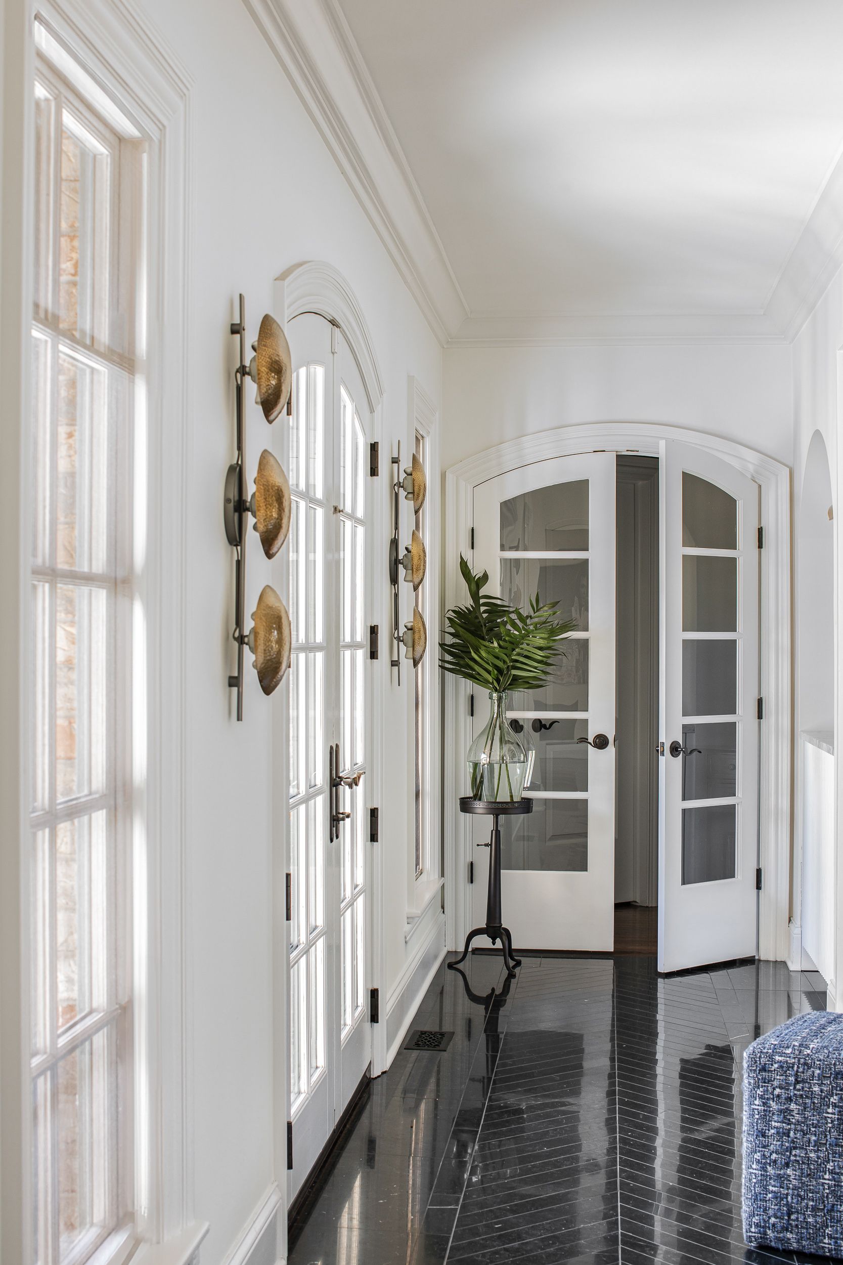 Bright hallway with French windows, brass wall sconces and arched glass doors.
