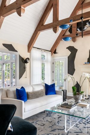 Contemporary living space with vaulted ceiling, exposed beams, and white sofa accented with blue pillows.