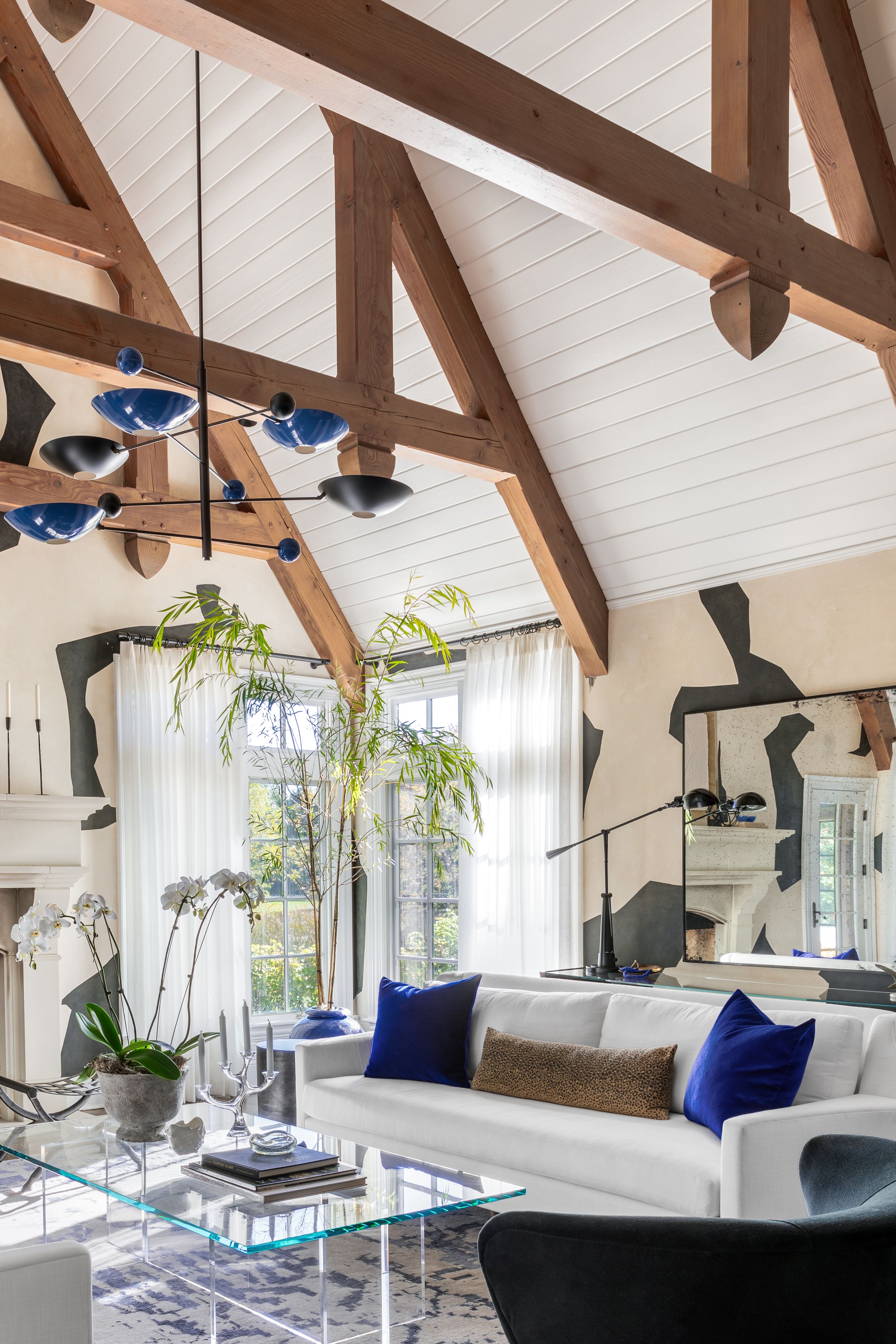 Luxurious living room with exposed wooden beams, blue pendant lights, and modern white furnishings.