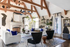Living room featuring abstract wall art, white sofas with blue pillows, and exposed wooden ceiling trusses.