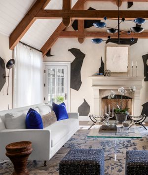 Stylish living area with geometric wall art, blue accents, and white furniture around a glass coffee table.