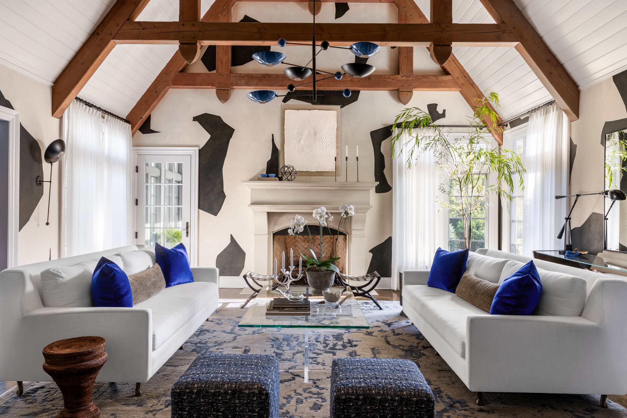 Modern living room with cathedral ceiling, white sofas, blue pillows, and distinctive black wall patterns.
