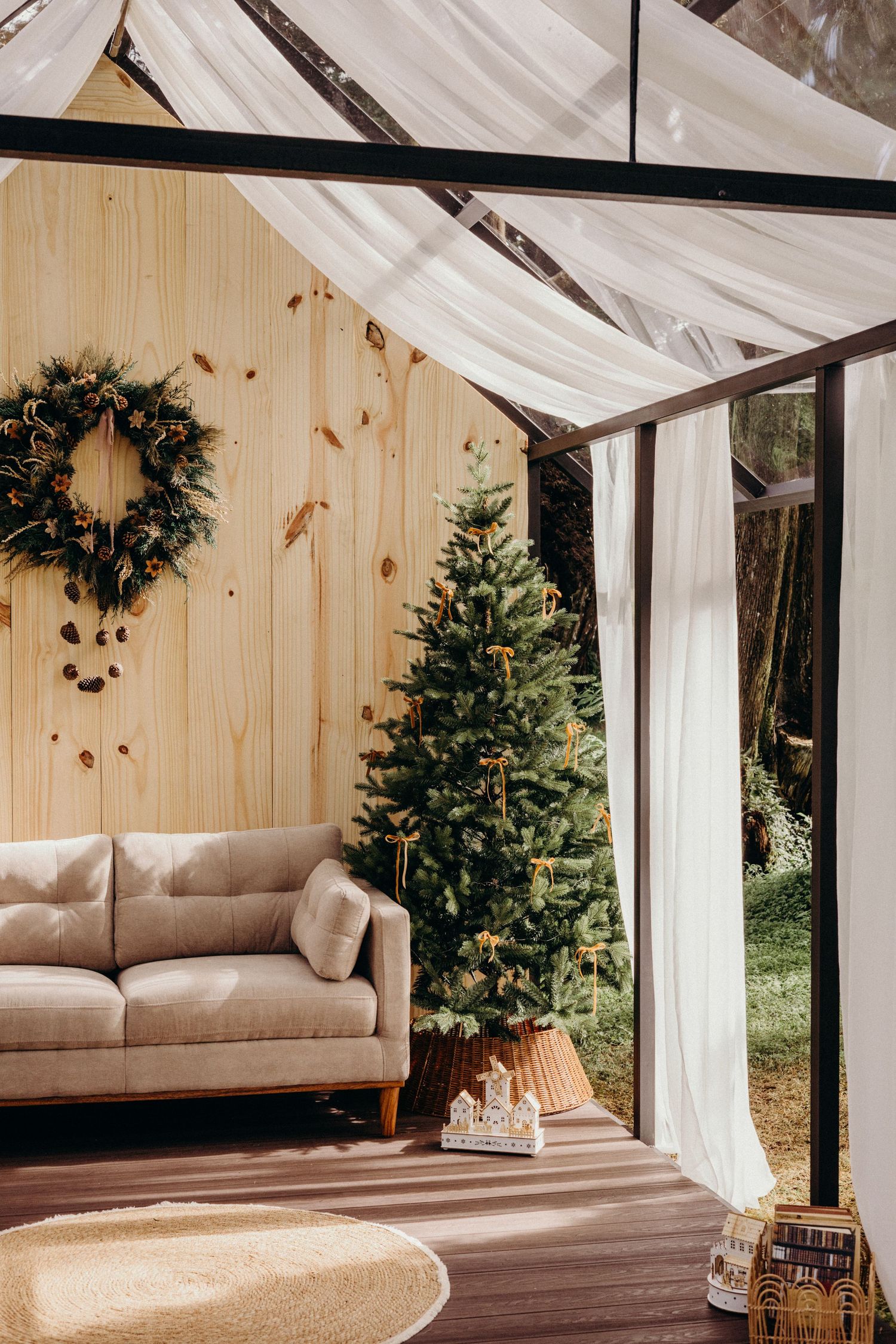 Cozy sunlit glamping tent interior with wooden walls, hanging plants, and a suspended beige daybed near white curtains.