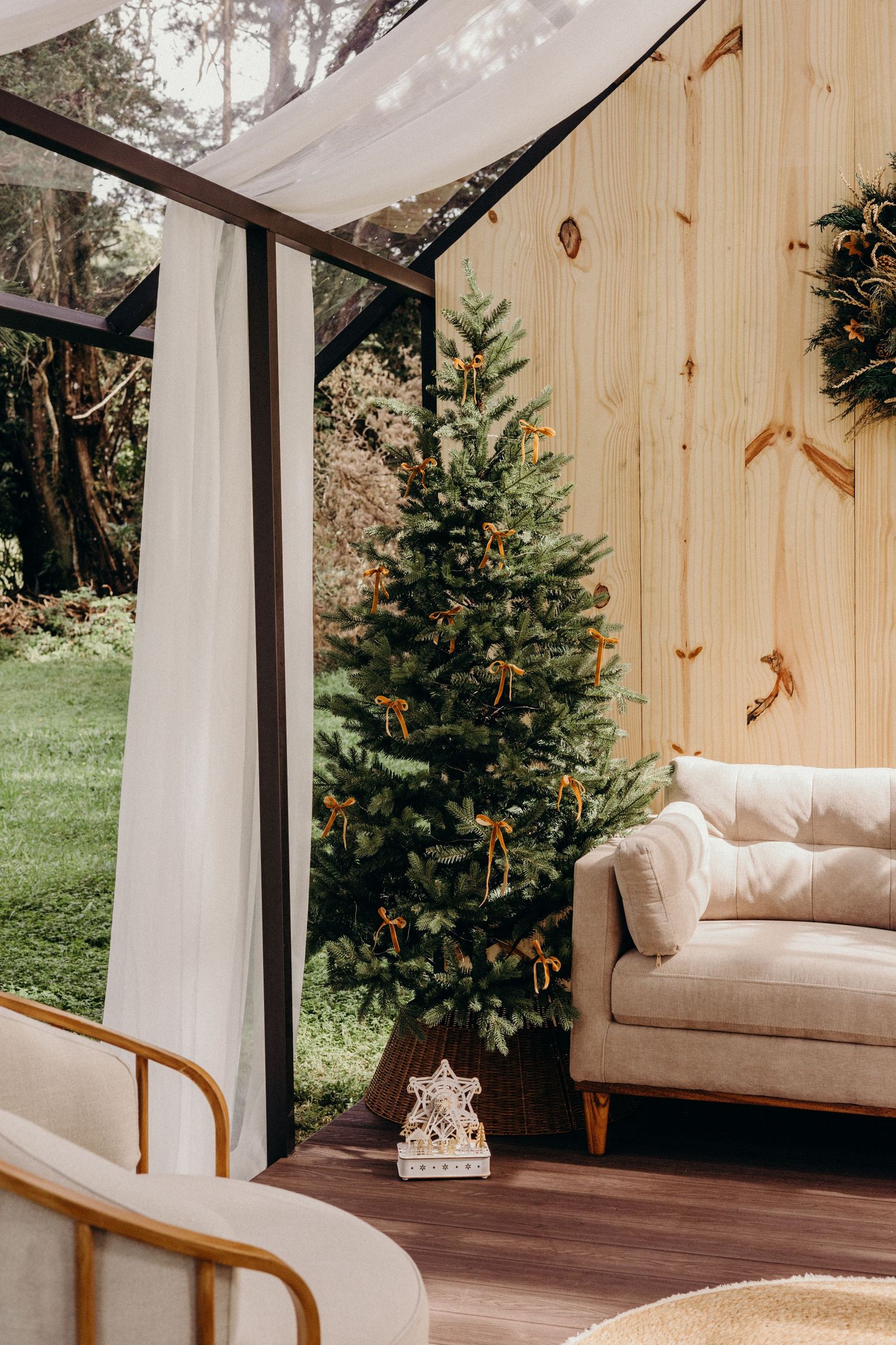 Modern sunroom interior with wooden walls features a cozy white sofa and decorated Christmas tree by large windows.