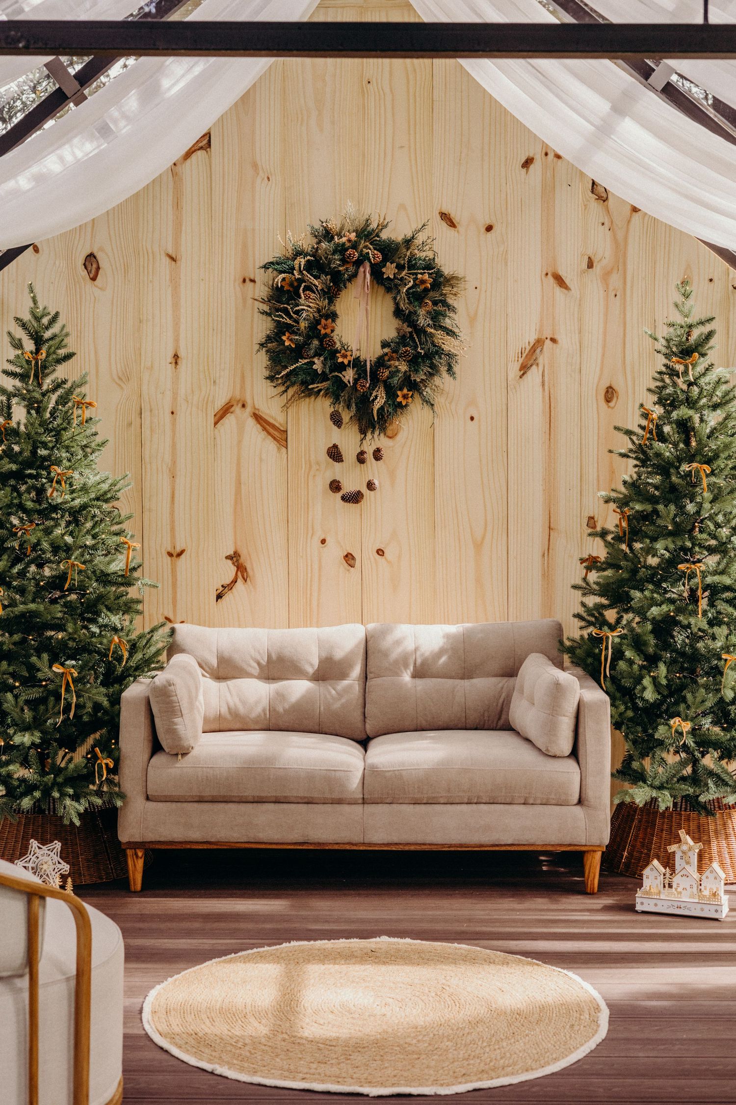 Modern beige sofa in a rustic wooden room decorated with Christmas trees and holiday greenery.