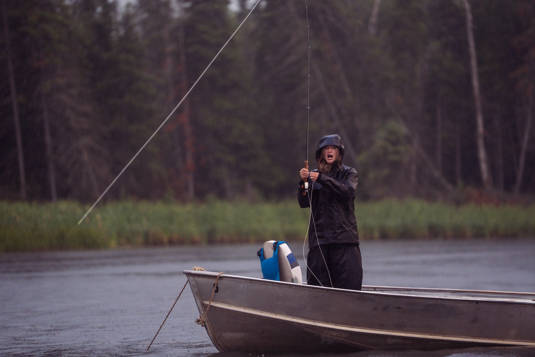 A person fishing from a small aluminum boat on a misty lake in a wooded area.