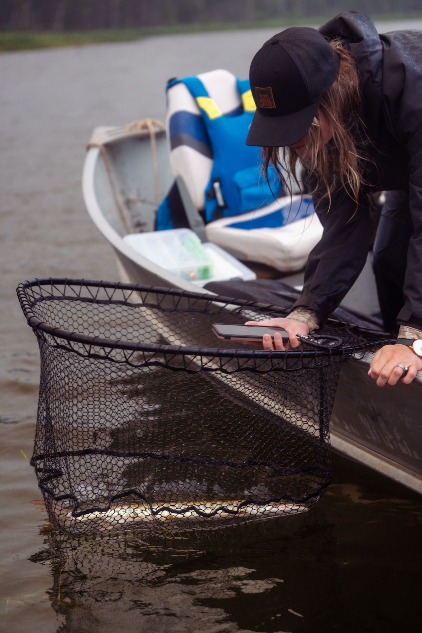 A person in a black cap leans over a boat to check a fishing net in dark waters.
