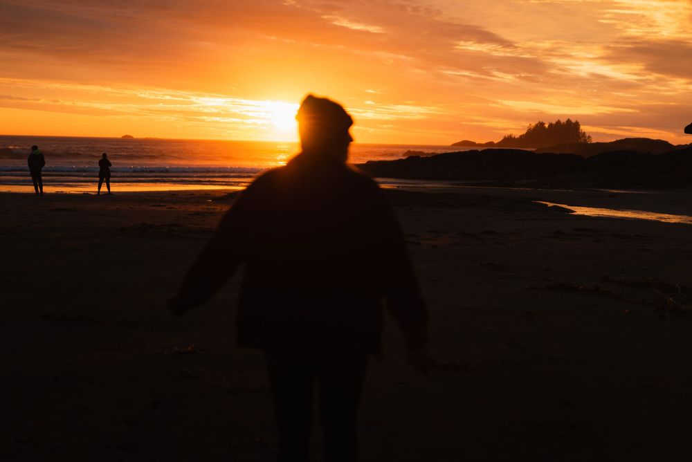 Silhouette einer Person läuft mit ausgebreiteten Armen einem strahlenden Sonnenuntergang am Meer entgegen