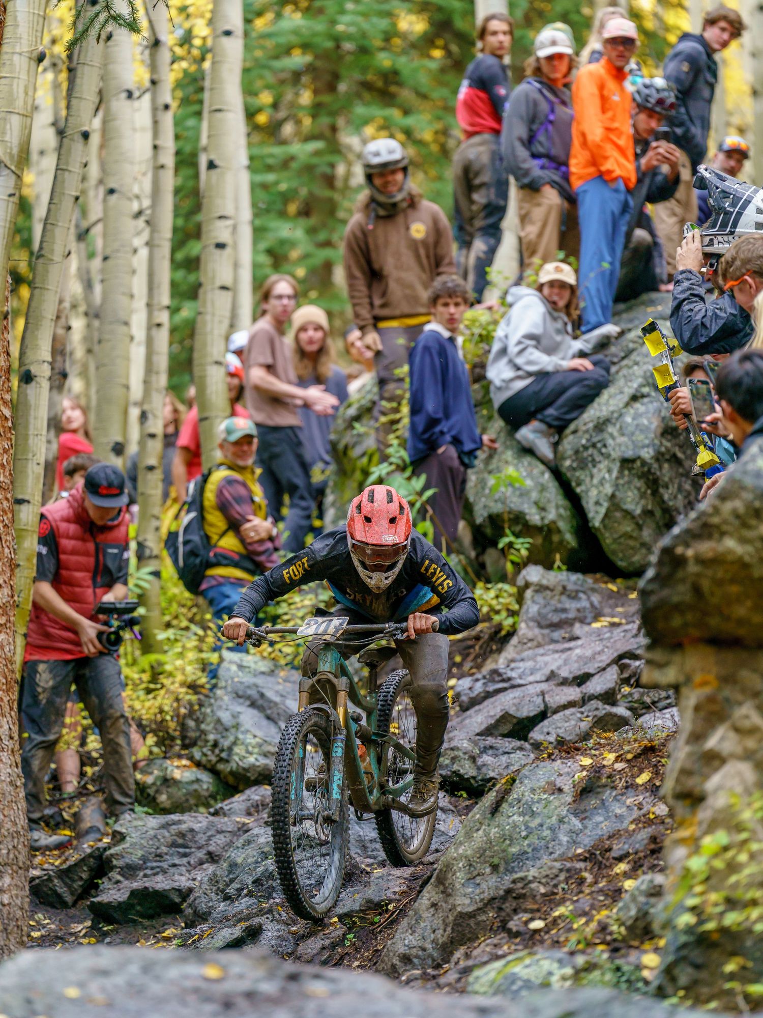 Mountain biker navigates rocky terrain while spectators watch from surrounding trail.