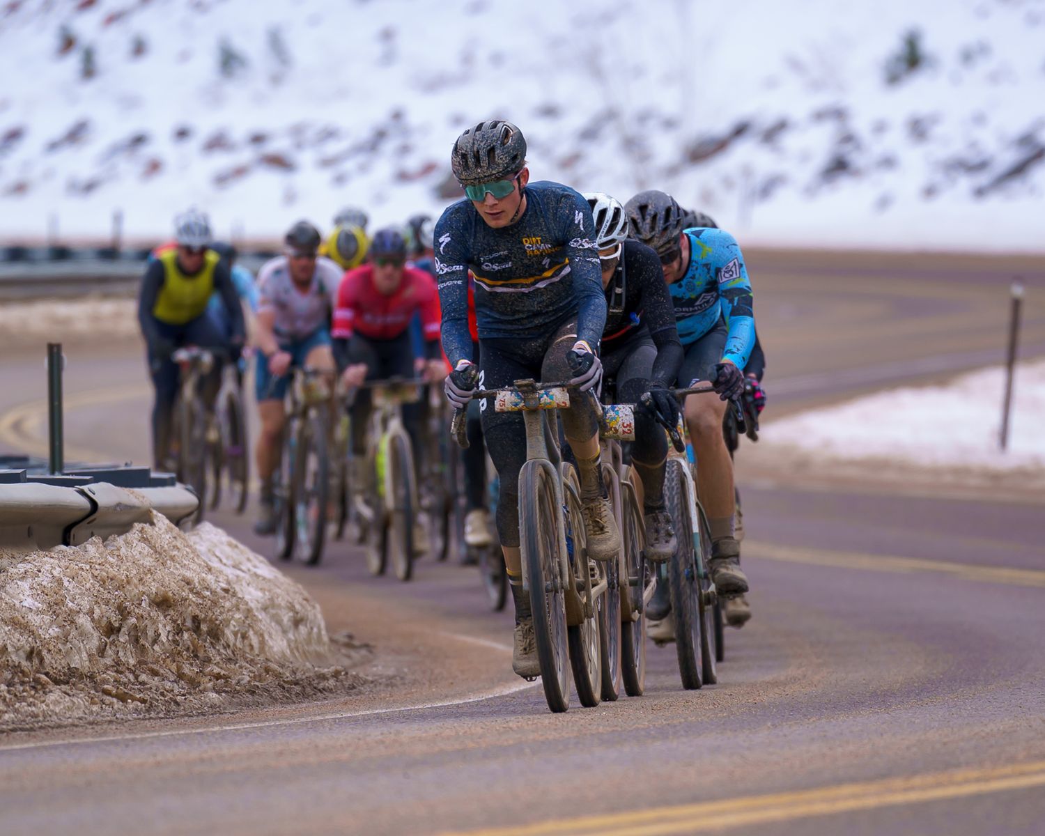 Cyclists racing on mountain road with snowy peaks in background.