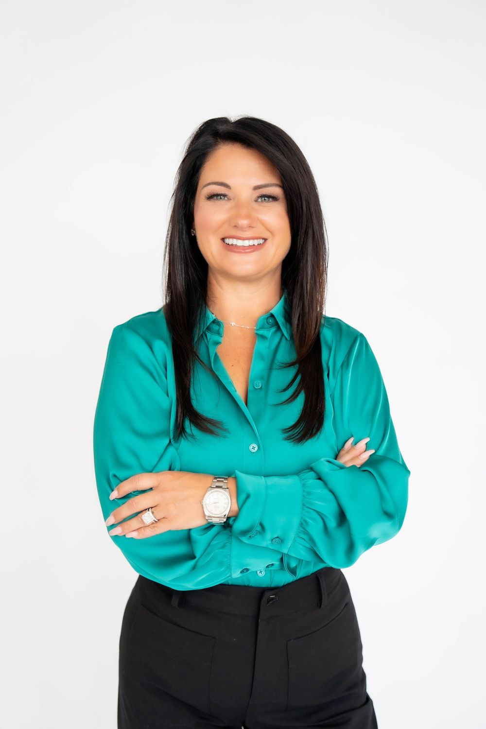 Professional woman in teal blouse with arms crossed, smiling confidently against white background.