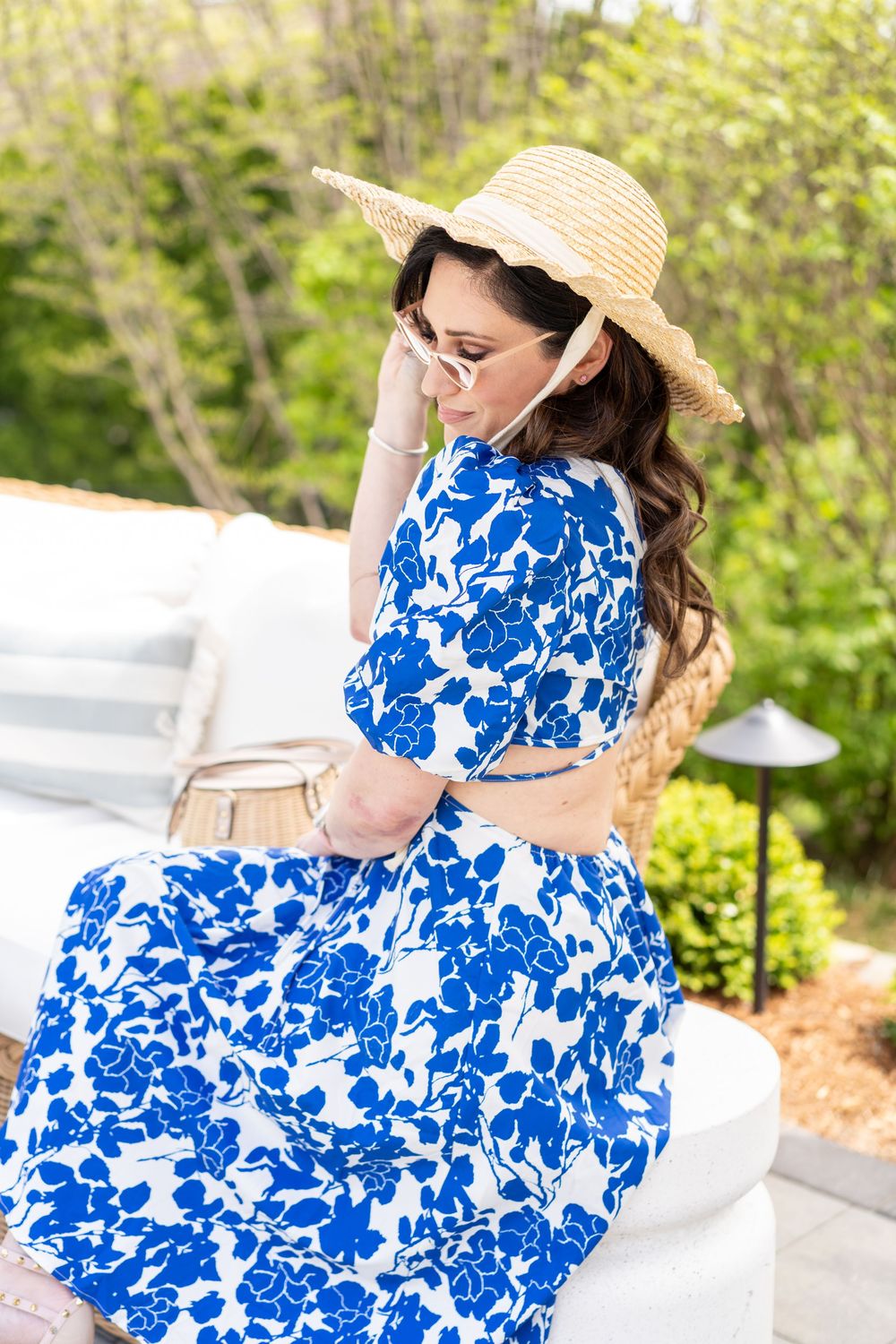 Relaxing on outdoor patio furniture in blue and white floral dress with straw hat.