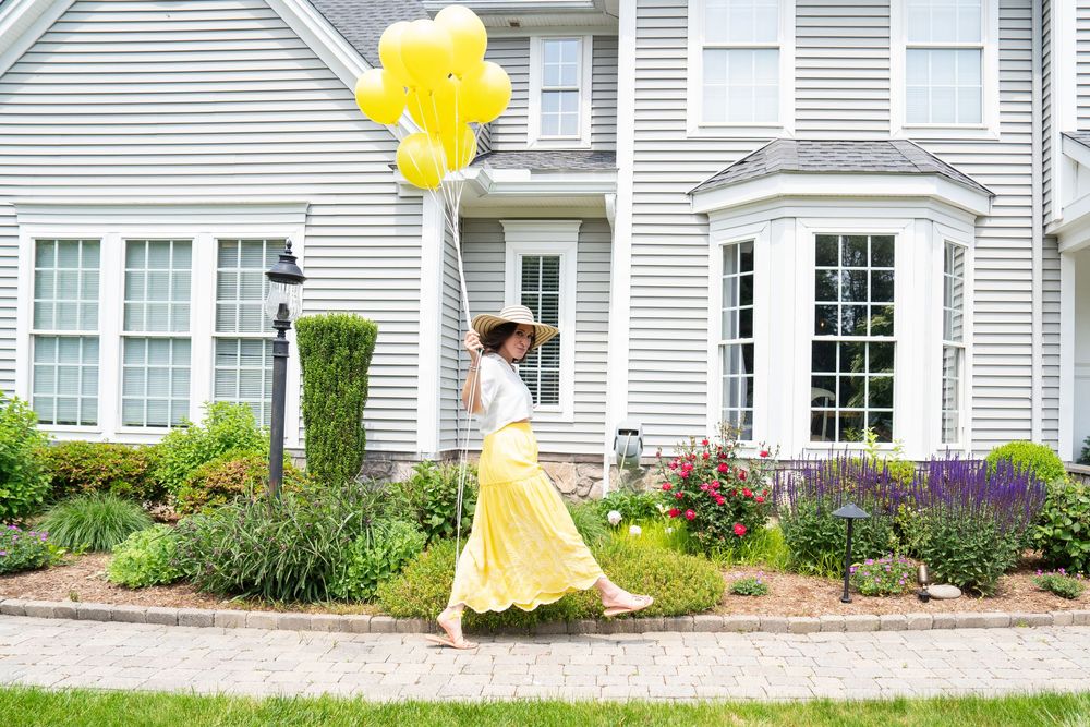 Yellow balloons float against gray siding of suburban homes on a sunny day.