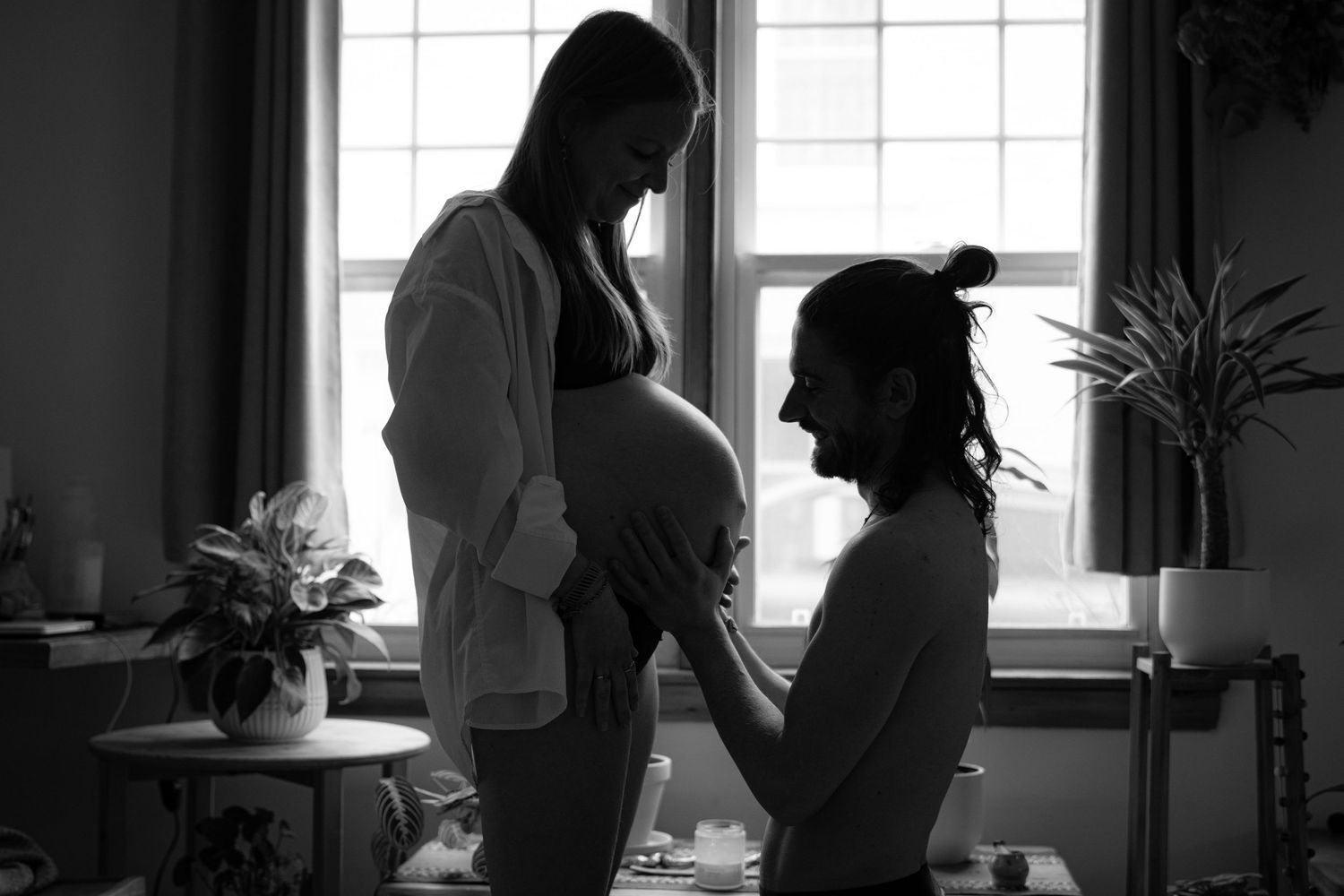 Black and white silhouette of pregnant woman and partner sharing intimate moment by window.