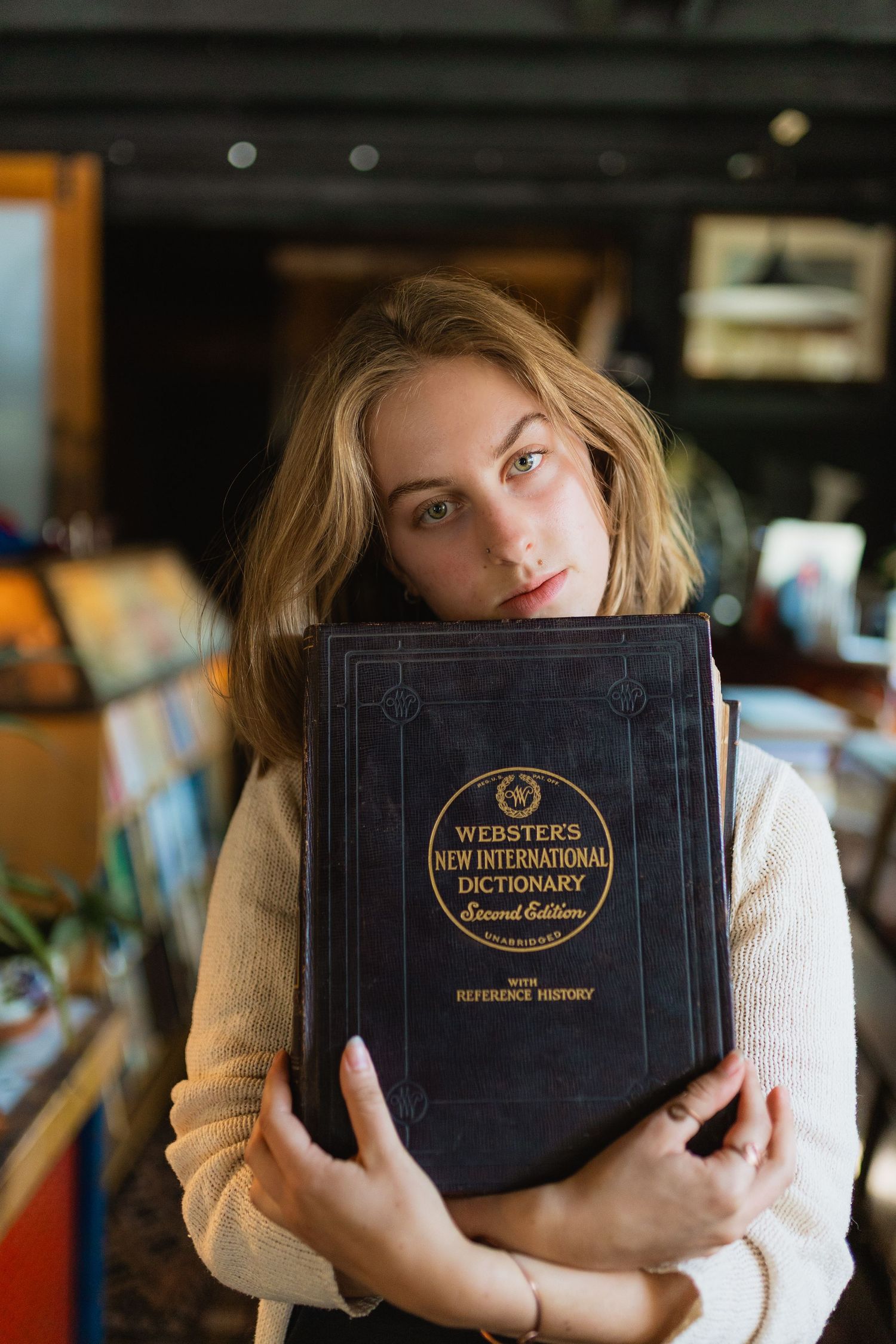Someone holds a large vintage Webster's New International Dictionary close to their chest while wearing a cream-colored sweater.