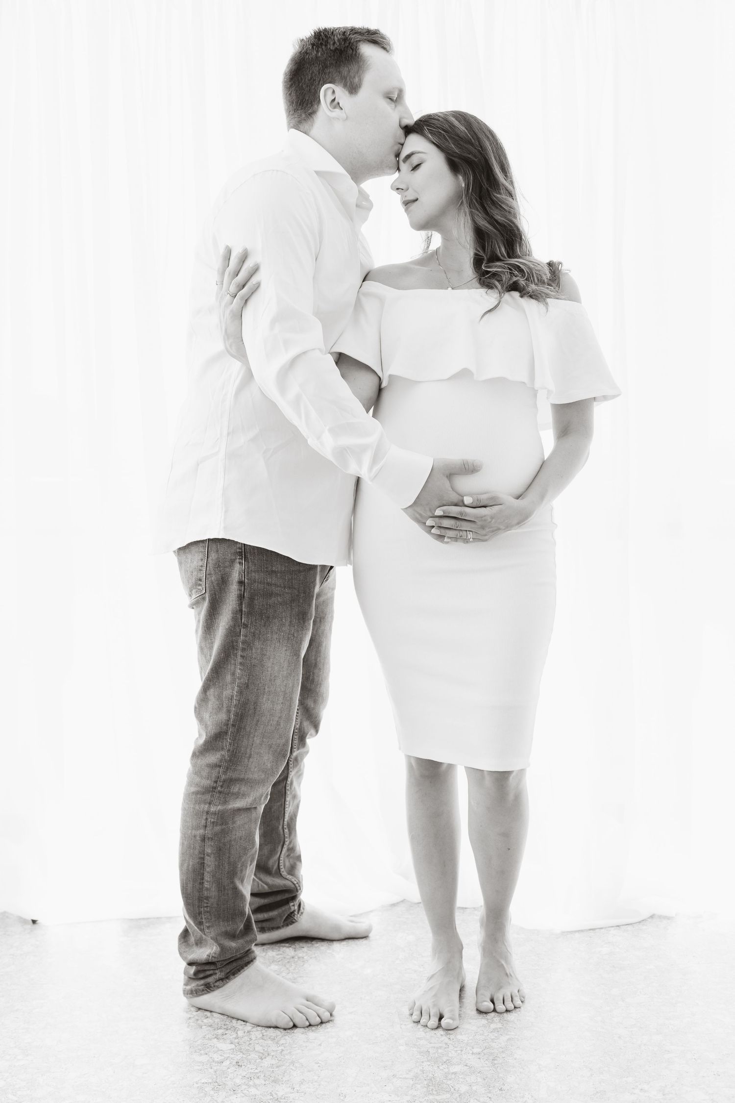 Black and white artistic maternity photo featuring an intimate moment between a couple in white outfits.
