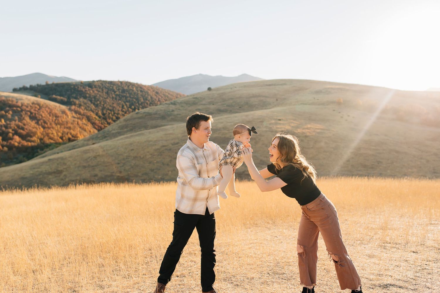 Three people playing together in a golden field at sunset with rolling hills in the background.