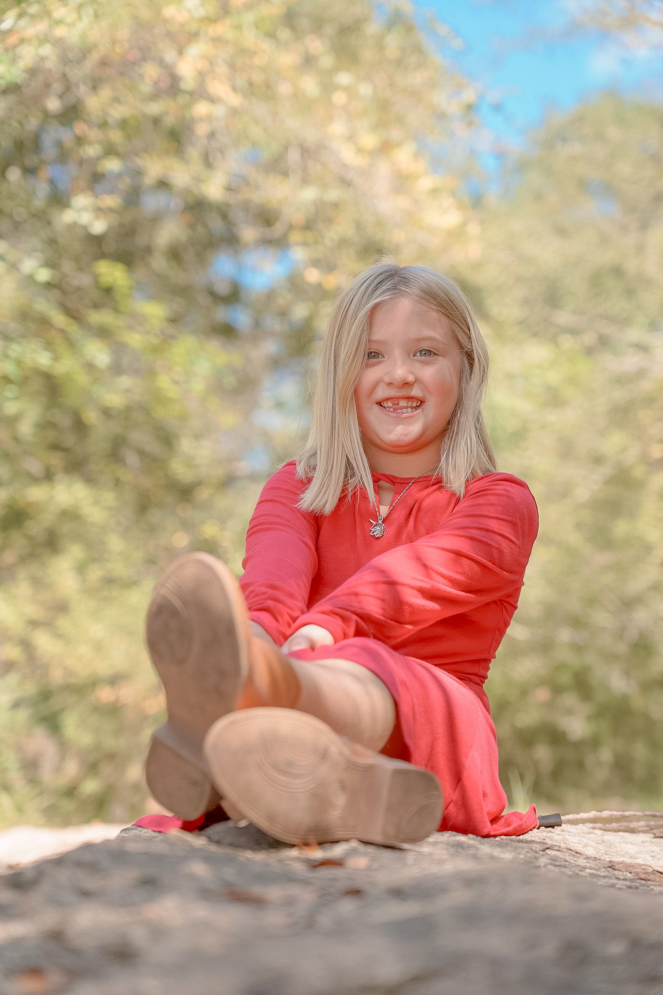 A person in a bright red dress sits outdoors with autumn foliage creating a soft, blurred natural backdrop. Lincolnton NC Family Photography