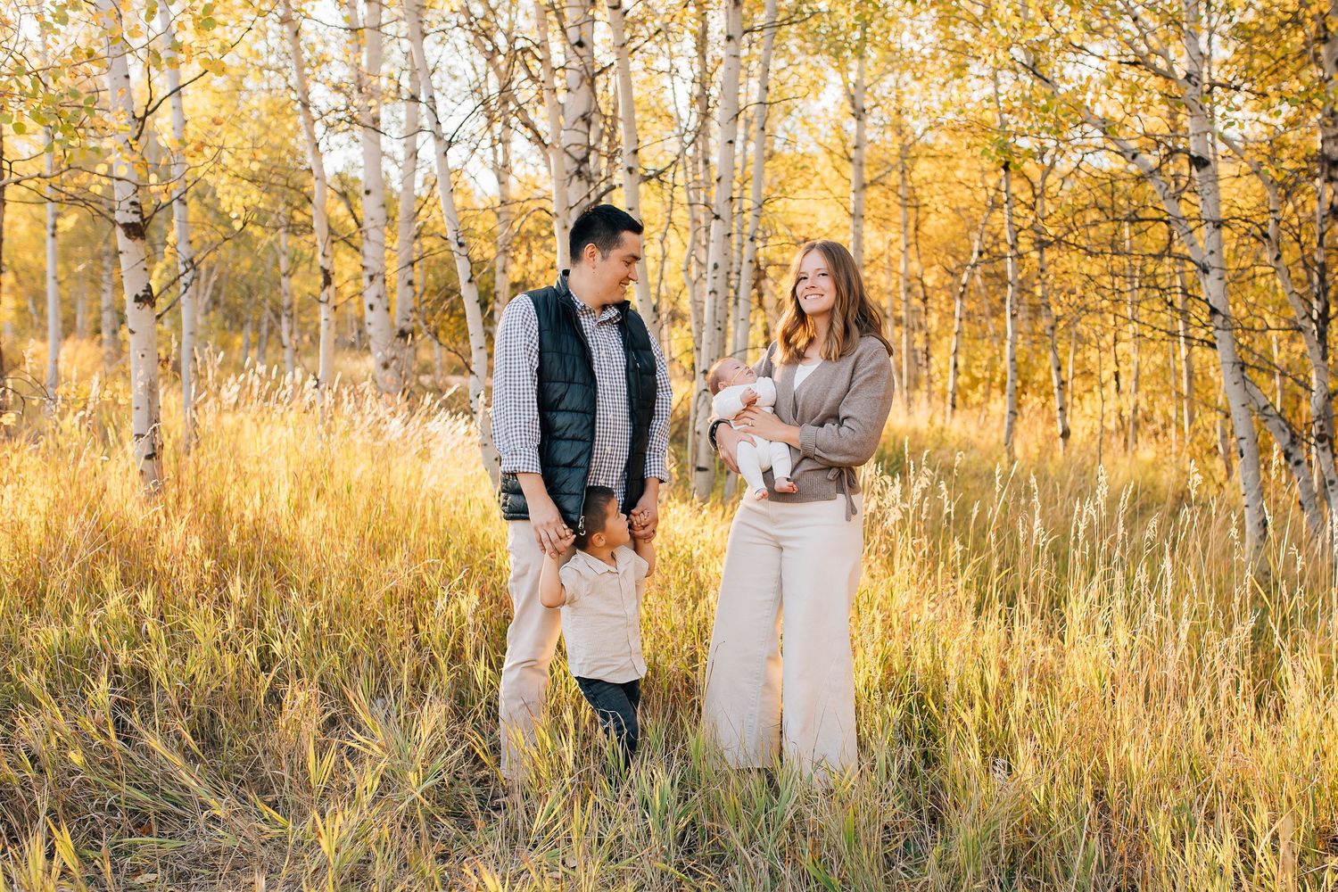 A small group stands together in a golden autumn field surrounded by aspen trees during sunset.