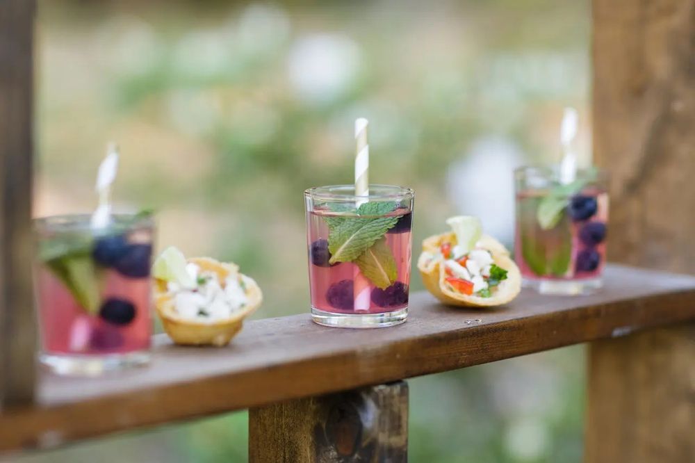 Colorful cocktails and appetizers arranged on a rustic wooden ledge with garnishes and artful presentation.